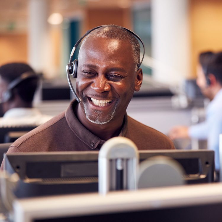 Mature Businessman Wearing Telephone Headset Talking To Caller In Customer Services Department